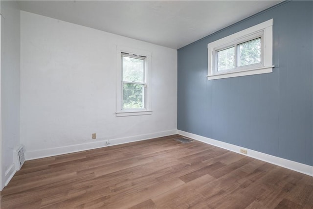 empty room with wood finished floors, a healthy amount of sunlight, and visible vents