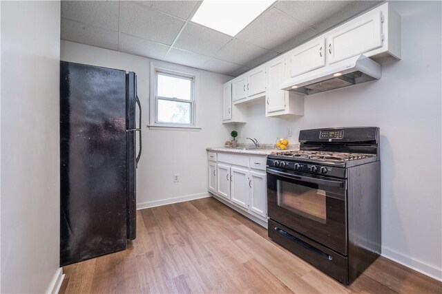 kitchen featuring black appliances, under cabinet range hood, a drop ceiling, white cabinets, and light countertops