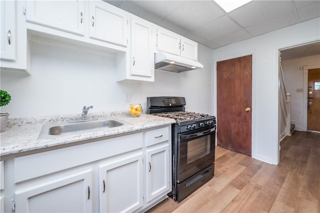 kitchen with light wood-style flooring, under cabinet range hood, a sink, white cabinetry, and black gas range oven