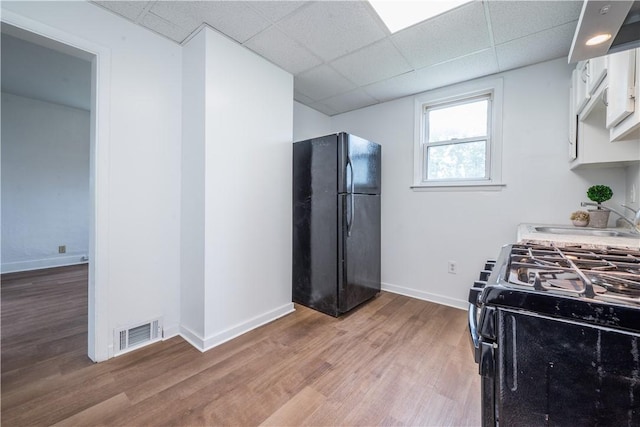 kitchen with baseboards, visible vents, light wood finished floors, a sink, and black appliances