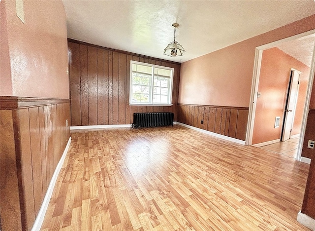 spare room with wood walls, radiator, light hardwood / wood-style floors, and a textured ceiling