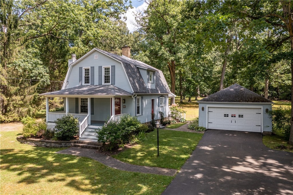 view of front of house with covered porch, an outbuilding, a garage, and a front lawn