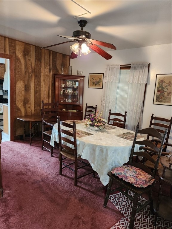 carpeted dining area with wooden walls and ceiling fan