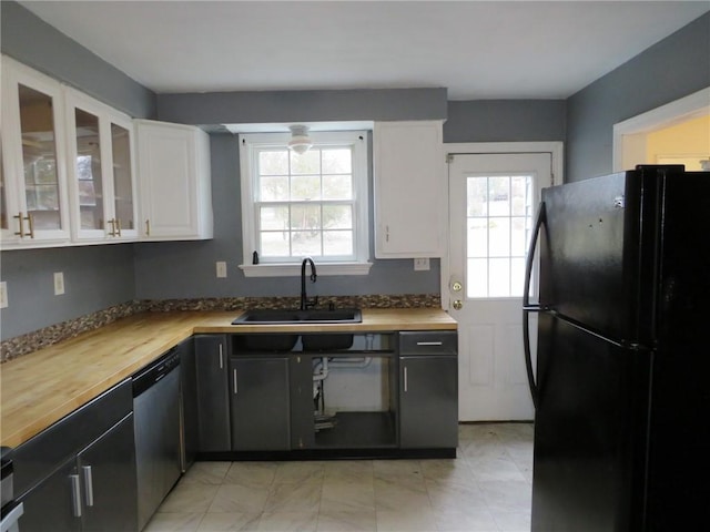 kitchen with stainless steel dishwasher, freestanding refrigerator, white cabinets, a sink, and wood counters