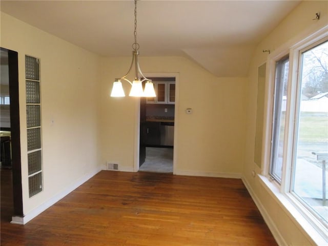 unfurnished dining area featuring baseboards, wood finished floors, visible vents, and an inviting chandelier