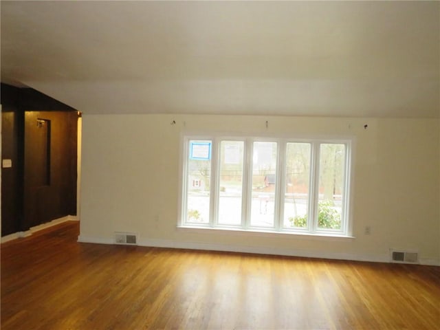 unfurnished room featuring vaulted ceiling, wood finished floors, visible vents, and baseboards