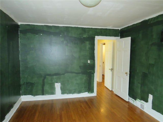 unfurnished room featuring baseboards, visible vents, and wood finished floors