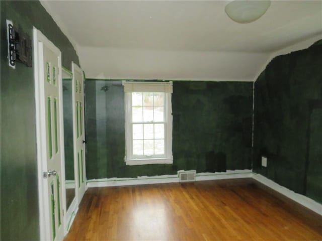 unfurnished room with lofted ceiling, visible vents, and wood finished floors