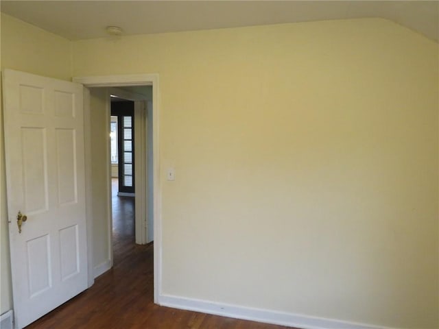 spare room featuring lofted ceiling, baseboards, and dark wood-style flooring