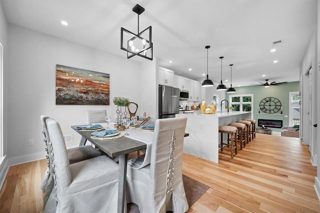 dining room with light wood-type flooring, sink, and ceiling fan with notable chandelier