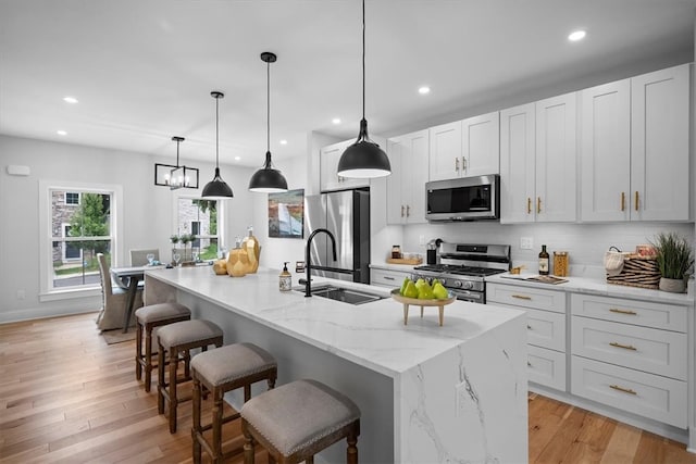 kitchen with light wood-type flooring, a center island with sink, decorative light fixtures, and appliances with stainless steel finishes