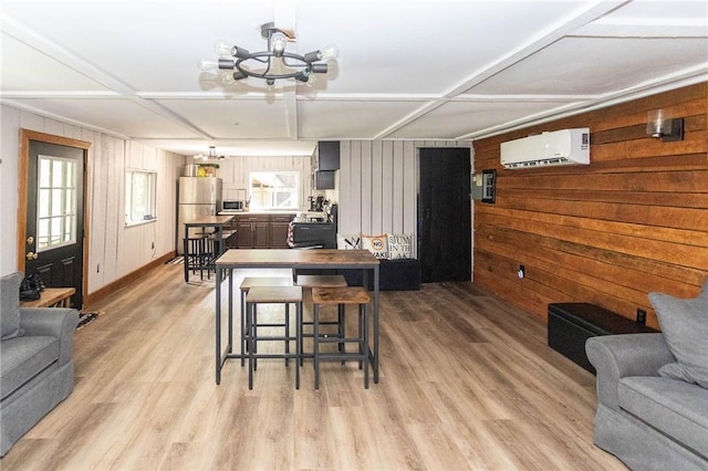 dining room featuring light wood-style flooring, an AC wall unit, baseboards, an inviting chandelier, and wooden walls