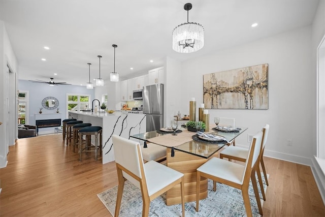 dining room with sink, light hardwood / wood-style flooring, and ceiling fan with notable chandelier