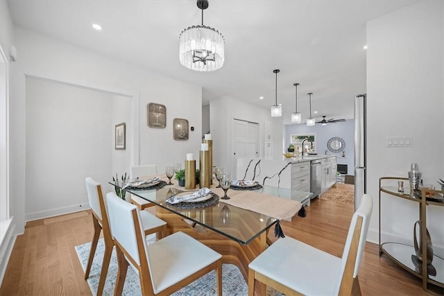 dining space with ceiling fan with notable chandelier, light hardwood / wood-style floors, and sink