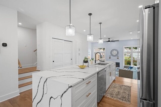 kitchen with stainless steel appliances, light hardwood / wood-style floors, light stone counters, a center island with sink, and white cabinets