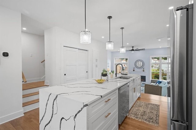 kitchen featuring white cabinets, stainless steel appliances, a center island with sink, and hardwood / wood-style floors