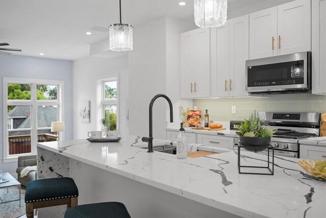 kitchen with appliances with stainless steel finishes, a notable chandelier, light stone countertops, and tasteful backsplash