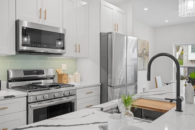 kitchen featuring appliances with stainless steel finishes, white cabinets, tasteful backsplash, and light stone countertops