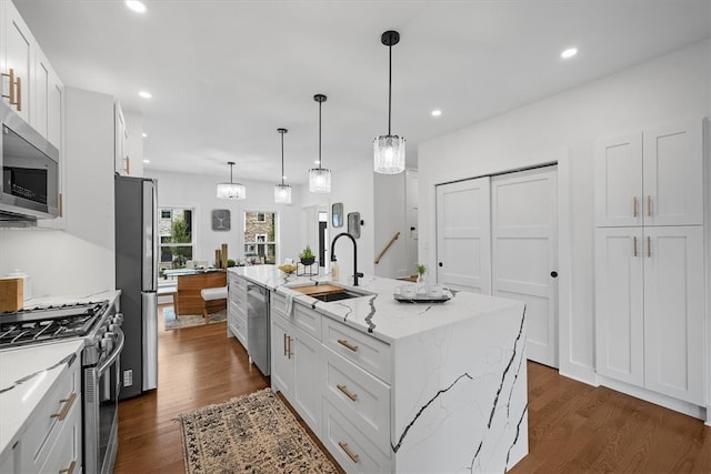 kitchen with stainless steel appliances, sink, an island with sink, white cabinets, and dark wood-type flooring