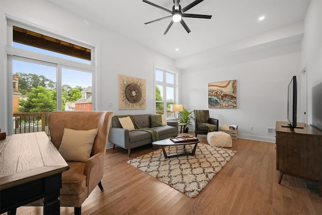 living room featuring a wealth of natural light, light wood-type flooring, a towering ceiling, and ceiling fan