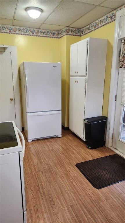 kitchen with white appliances, light hardwood / wood-style flooring, white cabinets, and a drop ceiling