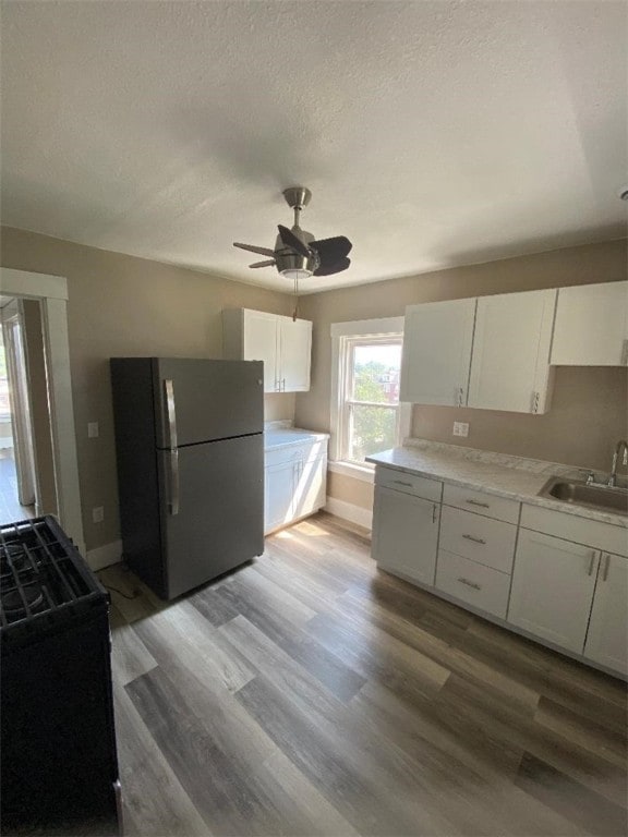 kitchen featuring white cabinetry, black range, light wood-type flooring, and stainless steel fridge