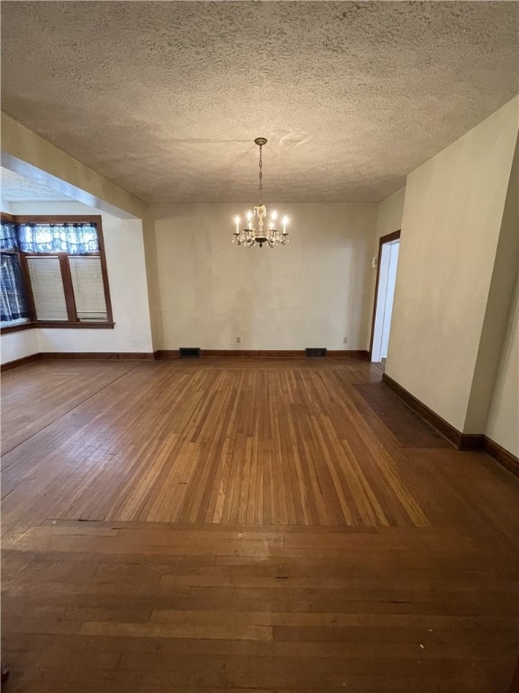 unfurnished room with a textured ceiling, dark wood-type flooring, and a notable chandelier