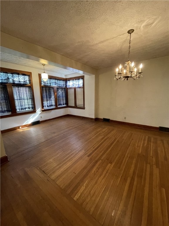 empty room with hardwood / wood-style flooring, a chandelier, and a textured ceiling