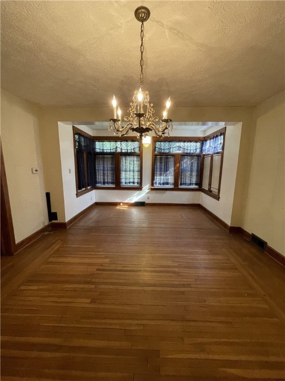 unfurnished dining area with a textured ceiling, dark wood-type flooring, and a notable chandelier