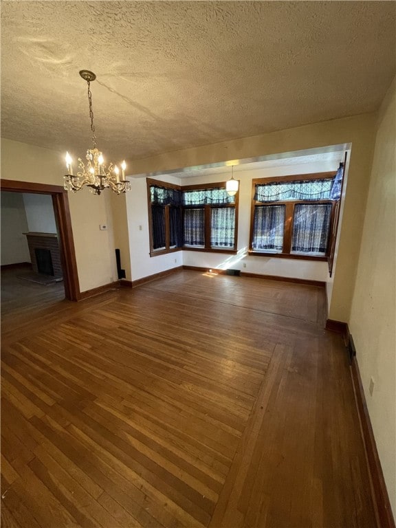 spare room with a fireplace, a textured ceiling, an inviting chandelier, and dark hardwood / wood-style floors