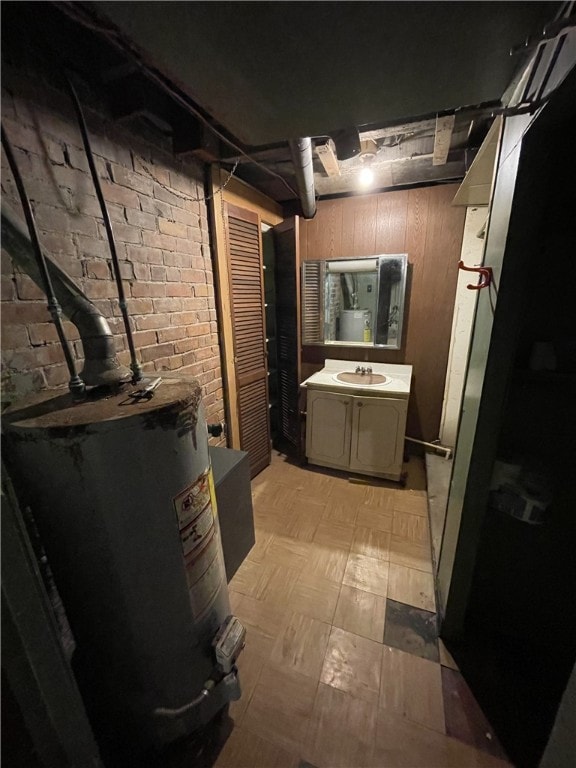 bathroom featuring vanity, water heater, and brick wall