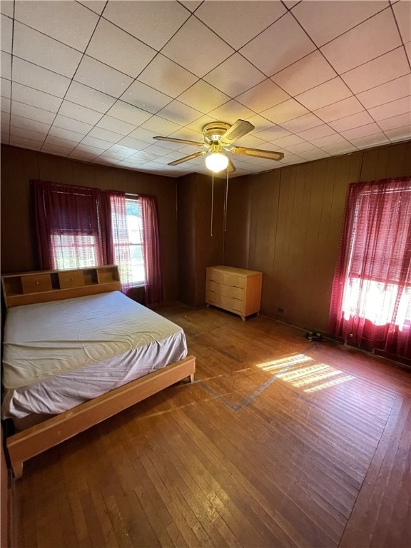 unfurnished bedroom featuring ceiling fan, wood walls, and hardwood / wood-style flooring