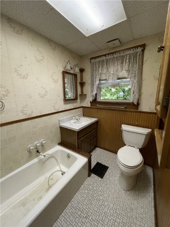 bathroom featuring a tub to relax in, toilet, a paneled ceiling, wood walls, and vanity