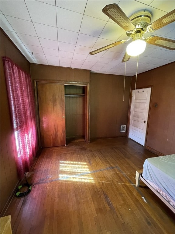 unfurnished bedroom featuring wood walls, ceiling fan, dark hardwood / wood-style floors, and a closet