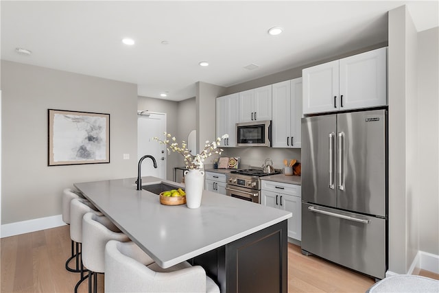 kitchen with light wood-type flooring, sink, an island with sink, and high quality appliances