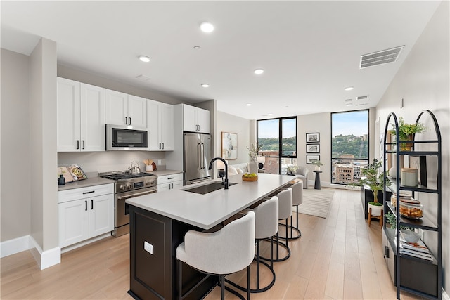 kitchen with sink, light wood-type flooring, premium appliances, a center island with sink, and white cabinets