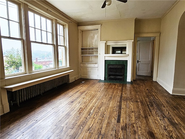 unfurnished living room featuring ceiling fan, radiator, dark hardwood / wood-style flooring, and a tiled fireplace