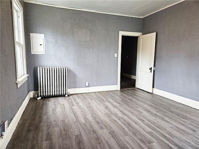 spare room featuring electric panel, ornamental molding, wood-type flooring, and radiator heating unit