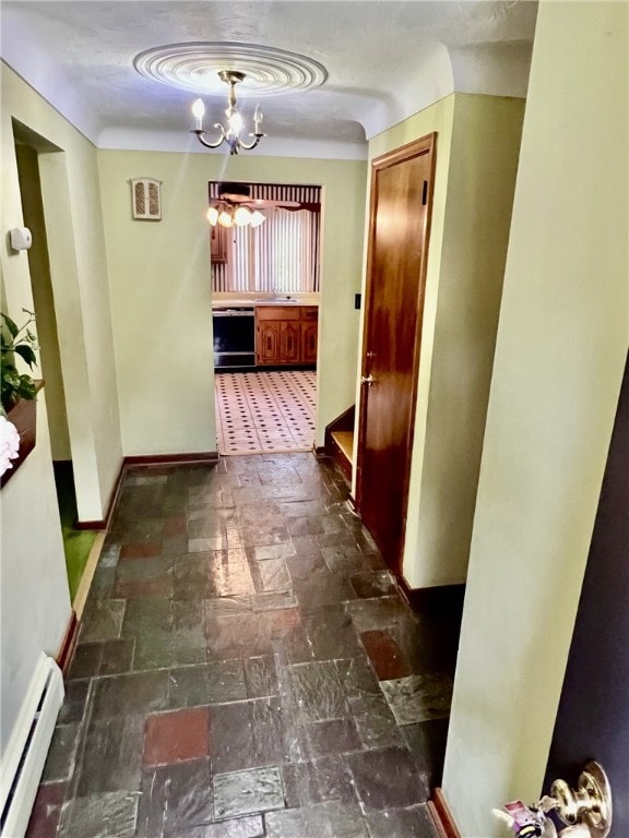 hallway featuring dark tile patterned flooring, baseboard heating, and an inviting chandelier