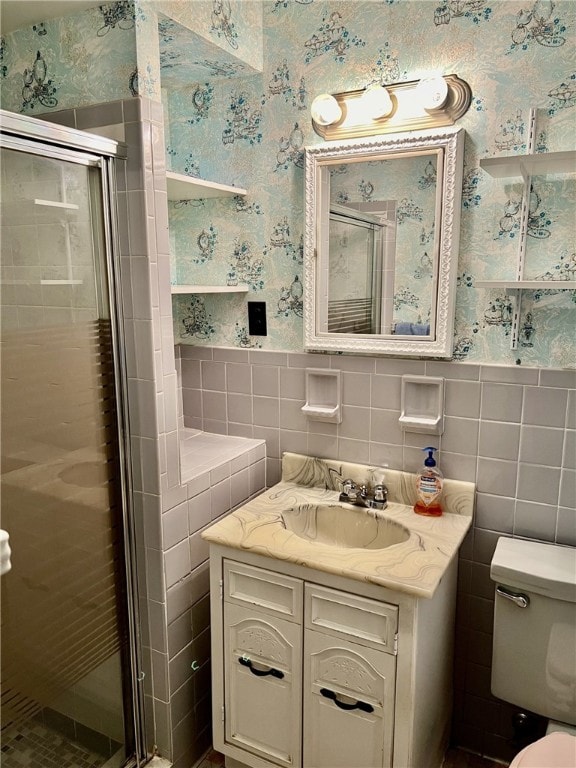 bathroom with a shower with shower door, toilet, vanity, and tile walls