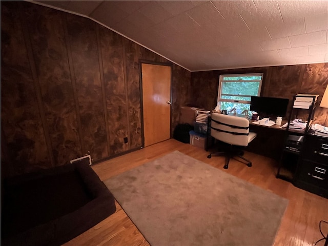 home office featuring wooden walls, light hardwood / wood-style floors, and vaulted ceiling