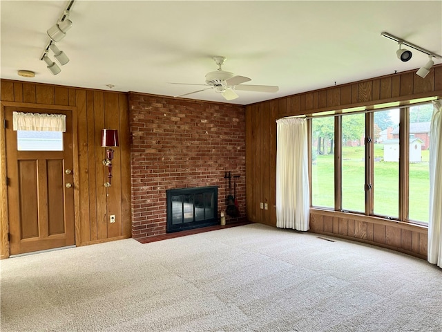 unfurnished living room featuring light colored carpet, rail lighting, wood walls, and a brick fireplace