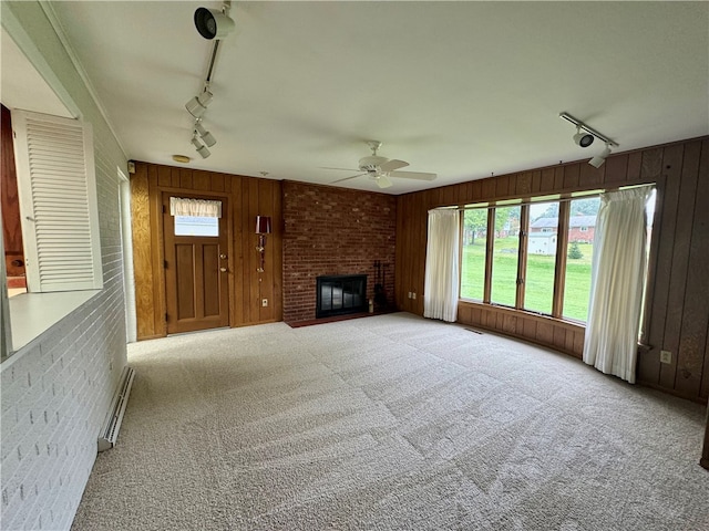 unfurnished living room featuring a fireplace, wood walls, baseboard heating, and track lighting