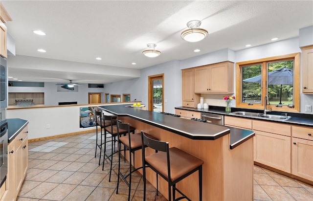 kitchen with dark countertops, a breakfast bar area, light brown cabinetry, and a sink