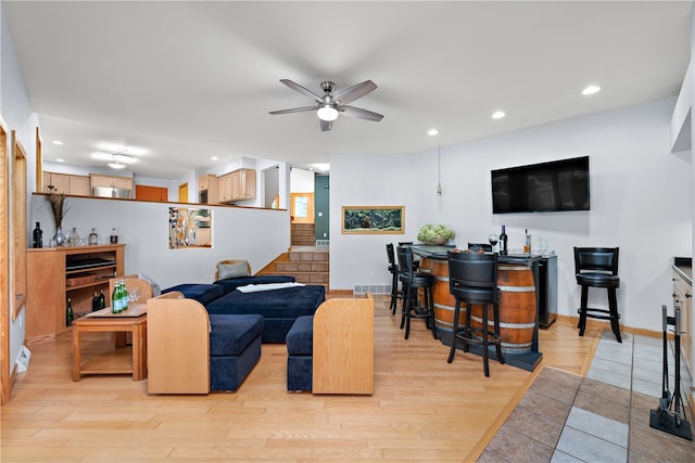 living room with light wood-type flooring, ceiling fan, and indoor bar