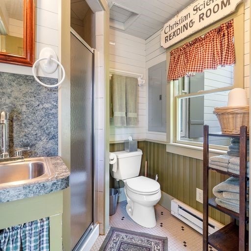 bathroom with a shower with door, a baseboard radiator, wooden walls, and toilet