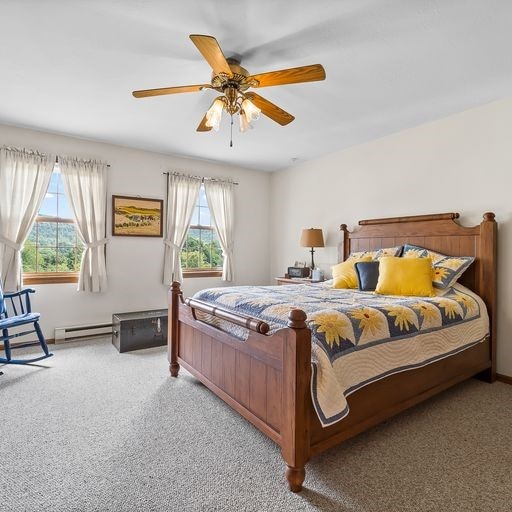 carpeted bedroom featuring baseboard heating, multiple windows, and ceiling fan