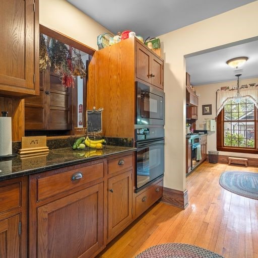 kitchen with stainless steel range, black microwave, light wood-type flooring, and dark stone countertops