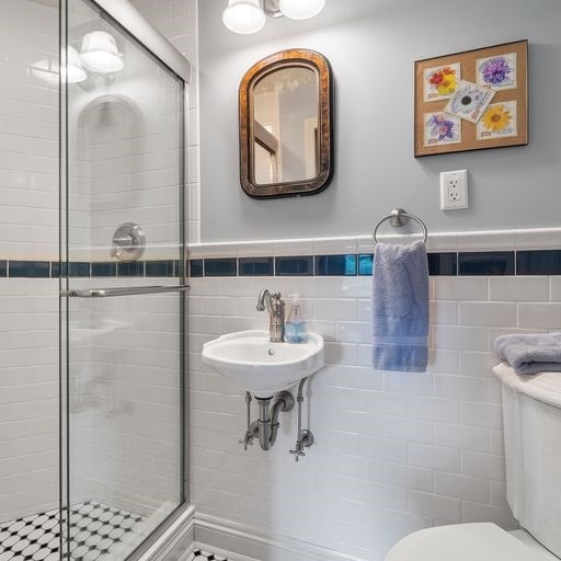 bathroom with toilet, tile walls, and a shower with door