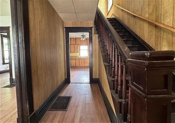 corridor featuring wood walls, a drop ceiling, and hardwood / wood-style flooring